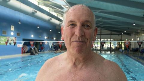 John stands by the side of a swimming pool.