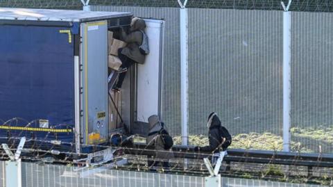 Migrants climbing into the back of a stationary lorry