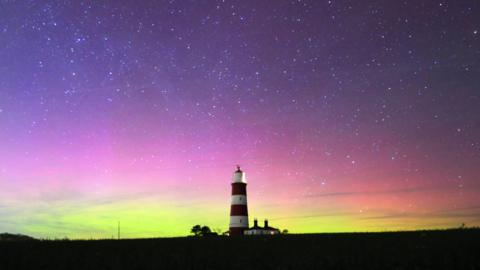 picture of a lighthouse with the night sky filled with greens, purples and reds of the northern lights.