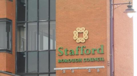 The outside of a brick building with windows on the left and the words Stafford Borough Council in green on the building in the centre and right of the photo.