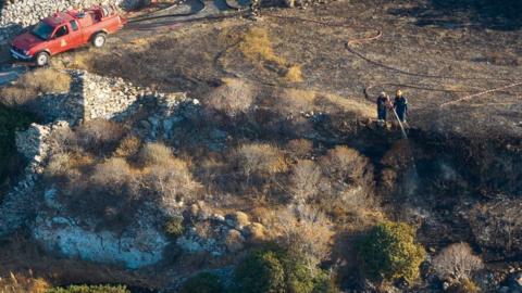 Firefighters hosing the crash sit on a hill side.