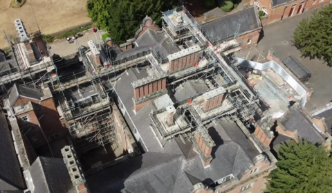 An drone-taken aerial view of scaffolding on top of a large red brick building