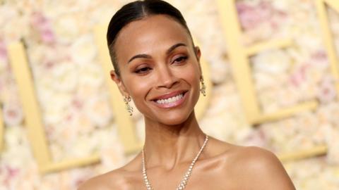 Zoe Saldaña attends the 82nd Annual Golden Globe Awards at The Beverly Hilton on January 05, 2025 in Beverly Hills, California. She is smiling and is wearing a diamond necklace and matching drop earrings. 