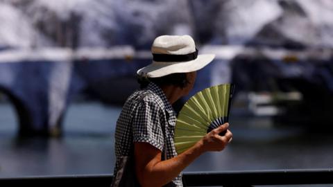  A person wearing a hat and holding a hand fan walks on the Pont des Arts bridge over the River Seine in Paris as temperatures rise during a heatwave affecting a large part of France, June 22,