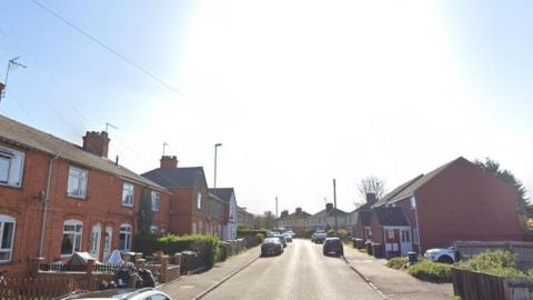 Trafford Road, in Rushden, Northamptonshire, showing a residential street with brick houses, and cars parked on the road