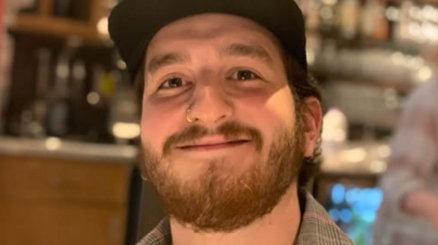 Barney Moorhouse is smiling. He is wearing a black baseball cap and a chequed shirt.