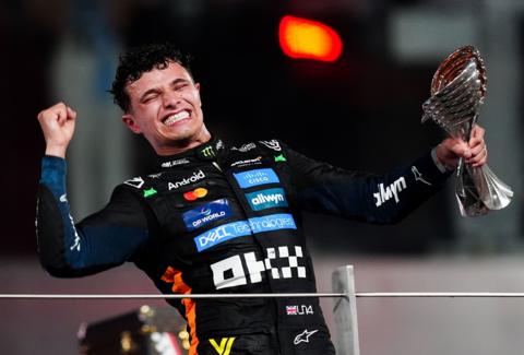 Lando Norris in his driver's outfit fist pumps the air while holding the F1 championship trophy