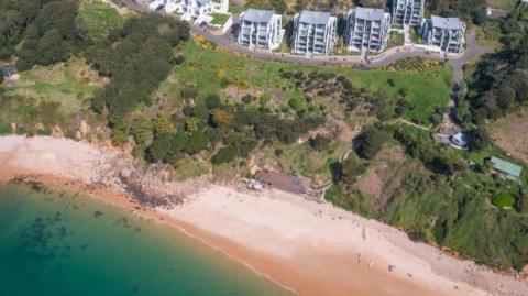 An aerial view of the beach and the cafe at Portelet Bay, with houses seen on the hill behind.