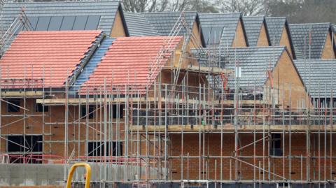 New homes under construction. There are three homes central to the image with scaffolding around them.