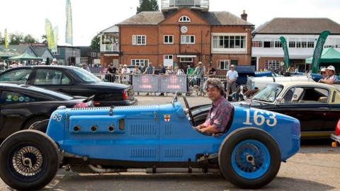 A man sat in a classic car. The car is blue and has large wheels and no windscreen.