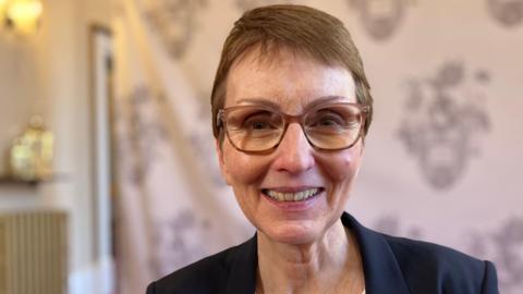 A recent photo of Helen Sharman smiling at the camera. She has short brown hair and is wearing rimmed glasses