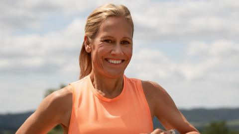Sophie Raworth smiling at the camera. She is wearing a neon orange tank top. 