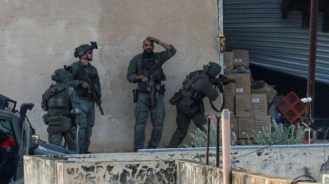 Israeli troops in Jenin take position behind a wall in front of a garage door before Palestinians emerge from it, in Jenin on Thursday