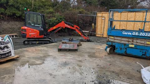 Obair togail air goireas ùr MRI aig Ospadal nan Eilean. Tha digear aig a' chùl agus làr concreig le uisge air, gun bhallachan an-àirde fhathast agus gun mhullach. 