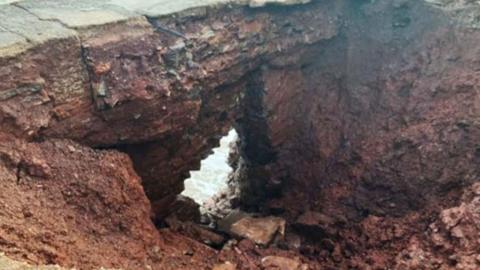 A large hole in the ground showing the sea visible through a gab in the rock.