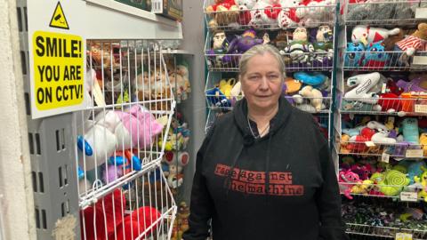 Gift shop owner Carolyn Tarlton in her store at Frenchgate Shopping Centre in Doncaster surrounded by cuddly toys and other gifts. There's a post on the wall which says 'Smile! You are on CCTV!'