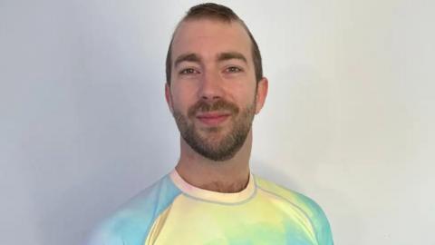 Will Stone has short brown hair and beard. He is wearing a colourful t-shirt