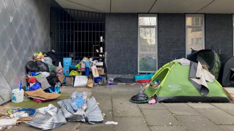A green domed tent next to piles of rubbish outside a metal gated alleyway 