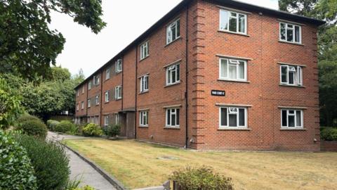 A red brick art deco style block of flats in Poole. The picture shows the front and side elevations. Lawn and shrubbery also pictured in the front garden.