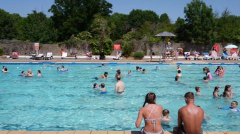 Two swimmers sit on the side of the pool watching people enjoy the water