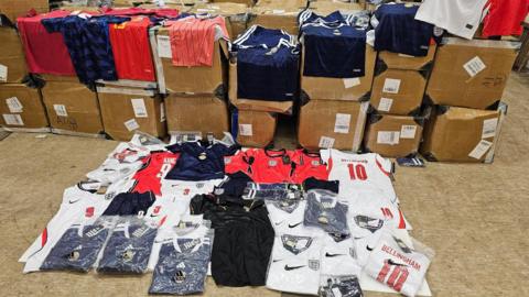 Dozens of fake Scotland and England strips laid out on boxes and on the floor of a warehouse