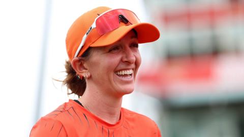 Kate Cross smiles, while wearing orange Sunrisers Leeds kit