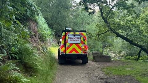 Mountain rescue vehicle drives down tight rural road with greenery on either side