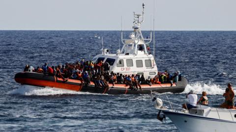 An Italian Coast Guard vessel carrying migrants rescued at sea passes near a tourist boat, on the Sicilian island of Lampedusa