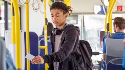 A young person on a bus holding a card to a bus ticket reader.