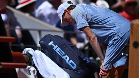 Jannik Sinner bends over next to his chair at a change of ends