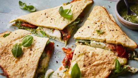 Four triangle quarters of a wrap with mozerella, pesto and tomato visible coming inside, scattered with basil.