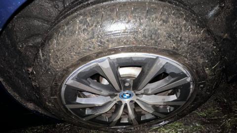 A burst tyre, standing on grass. You can see the deflated tyre and the wheel of the car. 