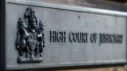A grey 'HIGH COURT OF JUSTICIARY' sign at the High Court in Edinburgh.