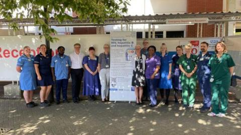 NHS staff standing next to sign about testing for HIV, hepatitis B and hepatitis C