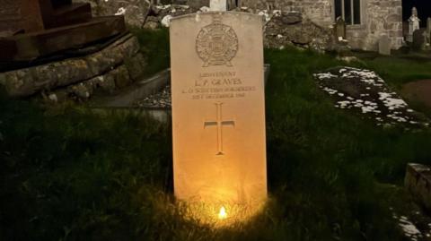 War grave lit up, behind it is a church