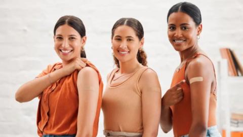 Three women with plasters on their left arms.