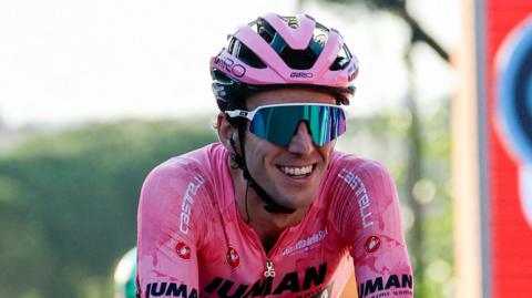 British cyclist Simon Yates smiles as he crosses the line in the leader's pink jersey to seal the 2025 Giro d'Italia title