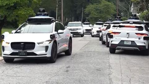A group of Waymo cars take up all the space in a street.