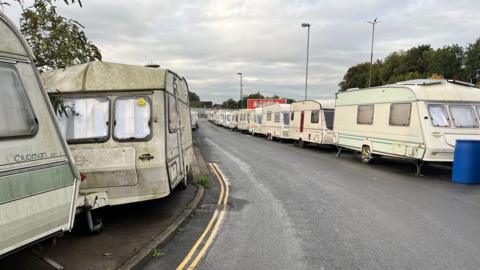 A number of dirty, dilapidated caravans parked up along the road end-to-end. 