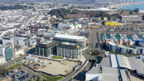 An aerial view of St Helier town with the sea and beach in the distance, rows of houses in view and the harbour.