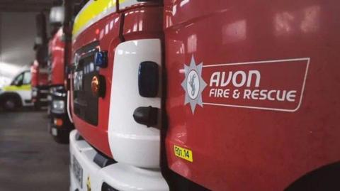 A close-up image of a red fire truck, that has a sign printed on the side reading 'Avon Fire and Rescue.'