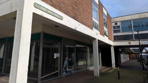Some dilapidated shopping units with a small green sign over them that says "The Maltings". 