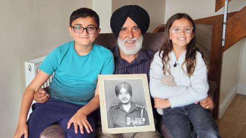 Children sitting with granddad with image of greatfather captain Gian Singh VC. 