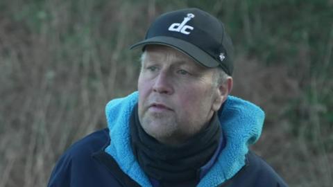 Paul Jackson wearing a black cap and navy and royal blue fleece jacket stands on land near where the former landfill site was located.