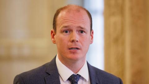Gordon Lyons is balding with reddish.brown hair and is wearing a suit