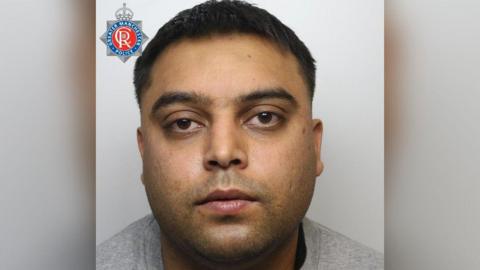 A mugshot of Waseem Ullah, who has short dark hair and brown eyes and is wearing a grey tracksuit, staring, expressionless at the camera.