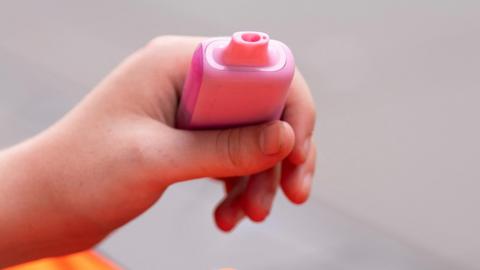 A hand holding a pink disposable vape