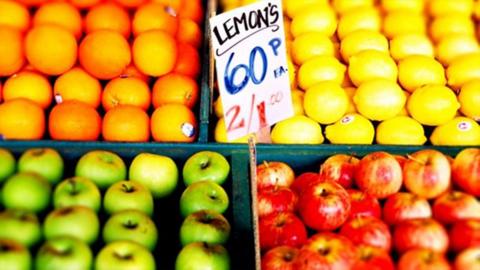 A fruit stall with oanges, lemons, and apples with a price sign in white