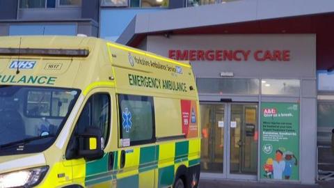 An ambulance is waiting at a bay beside the emergency department doors.