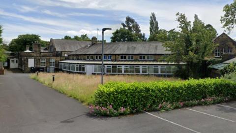 A large two-storey building surrounded by overgrown grass.